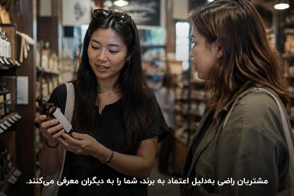زنی جوان در حال توضیح در مورد محصولی در دست برای شخص دیگر در فضای داخلی فروشگاه