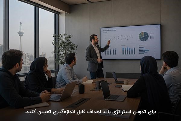 مدیر ایستاده در حال توضیح نمودارها در نمایشگر بزرگ و اعضای تیم نشسته دور میز در حال مشاهده