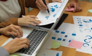 تیم کارشناسان در حال تحلیل نمودارها و داده‌های آماری با لپ‌تاپ در پروژه داده کاوی