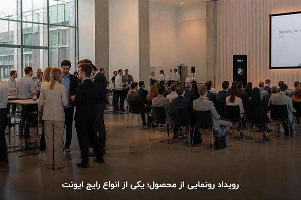 ایونت در حال برگزاری و افرادی نشسته و تعدادی ایستاده در فضای داخلی