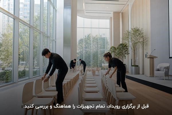 افرادی با لباسهای مشکی در حال مرتب کردن صندلیها تجهیزات در فضای برگزاری رویداد