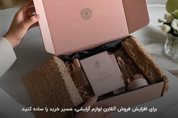 دست شخصی در حال باز کردن جعبه صورتی پر از لوازم آرایشی روی میز سفید